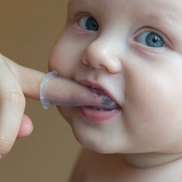 Baby gently biting finger with plastic infant toothbrush on it