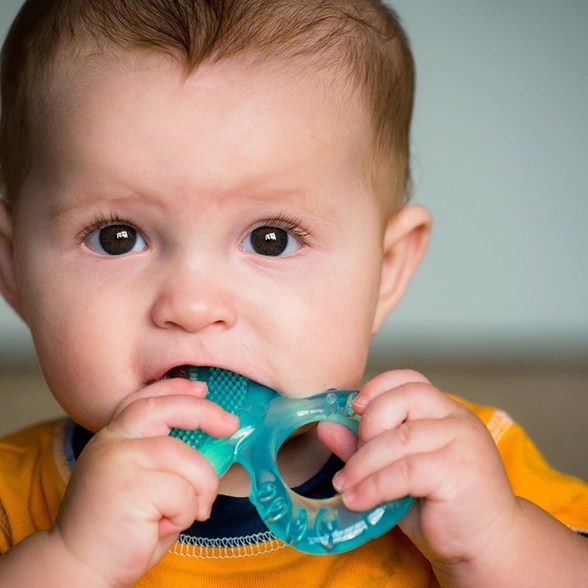 Baby boy in yellow shirt chewing on plastic teething toy