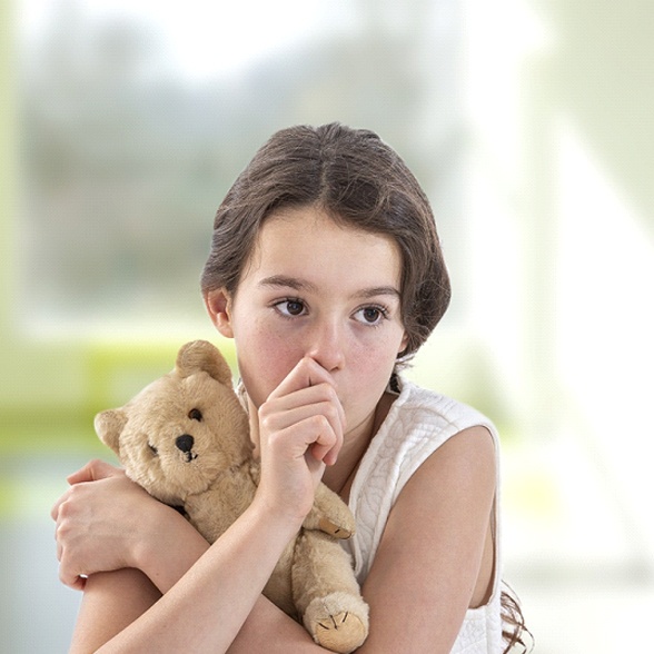 A girl holds a teddy bear and sucks her thumb while looking off in the distance