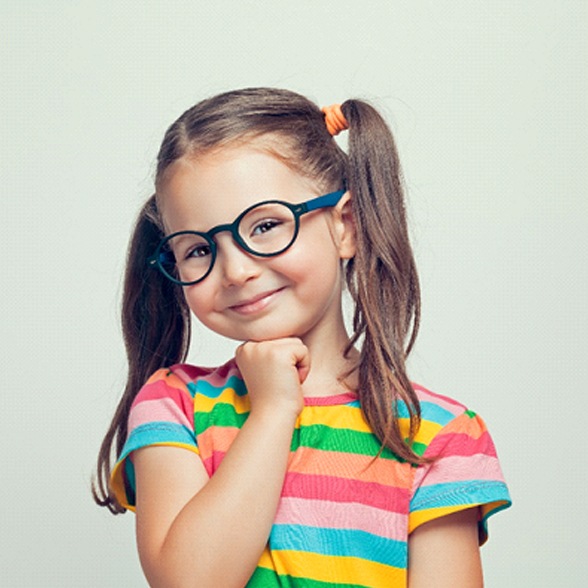 A little girl wearing a striped shirt and glasses smiles in preparation for seeing her dentist