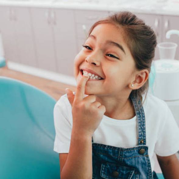 Young girl in dentist’s chair pointing at a tooth
