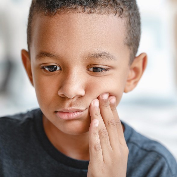 Child in need of emergency dentistry holding cheek in pain