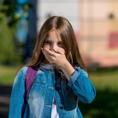 Little girl with lost dental crown covering her mouth