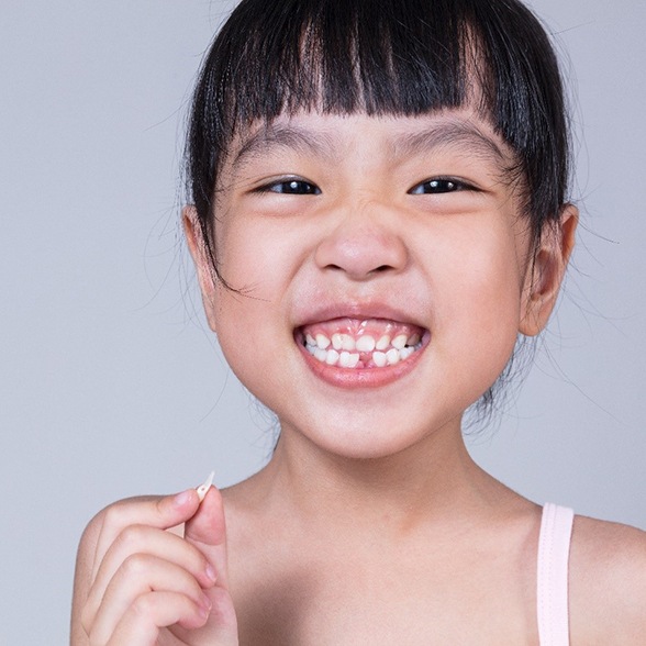 A little girl holding a tooth in her right hand while showing off the gap in her smile