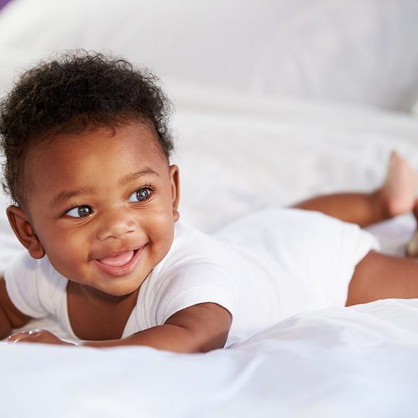 Happy baby in white bodysuit smiling after successful frenectomy