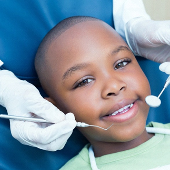A smiling African American boy next to gloved hands holding dental tools