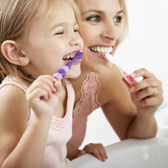 Mother showing daughter how to brush her teeth