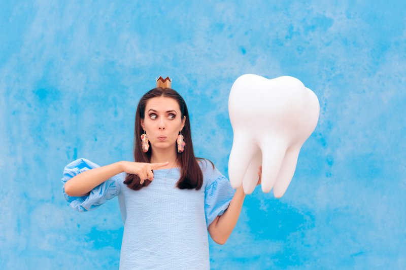 a woman wearing a crown and holding a big tooth and looking like the tooth fairy 