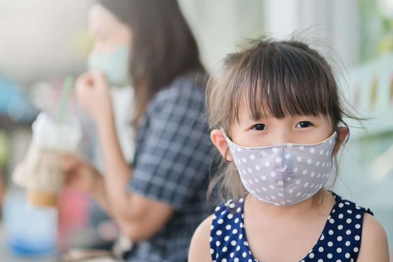 a little girl wearing a gray polka dot mask out in public