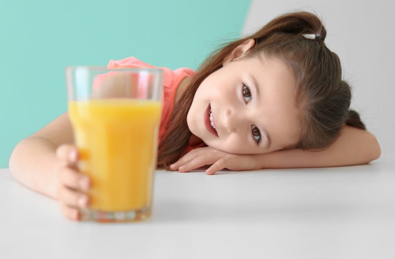 Girl smiling, resting head on table while holding a glass of orange juice