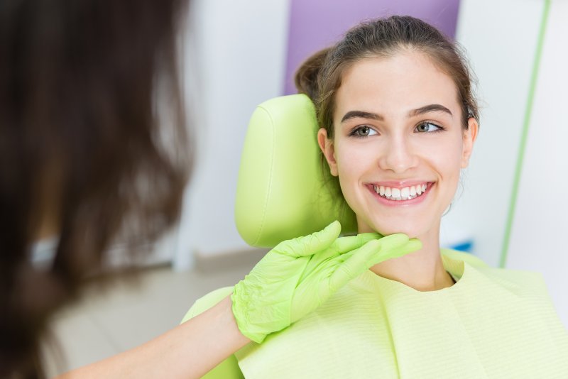 Teenage girl sitting in lime green dentist chair smiling with teeth at her off screen dentist who is wearing matching latex gloves