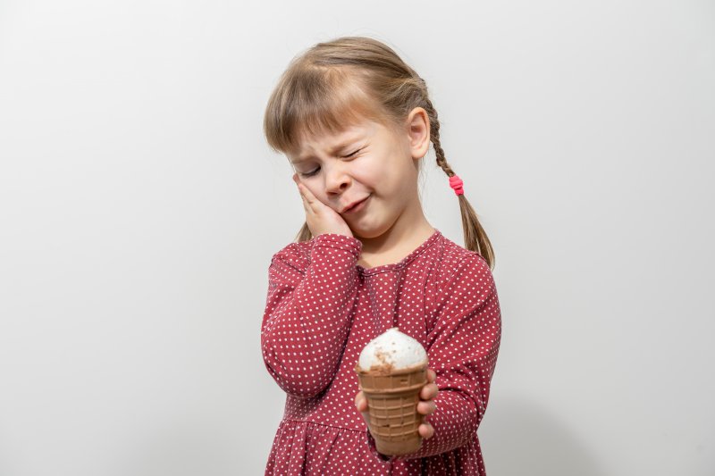 A child holding her cheek while trying to eat ice cream with tooth sensitivity