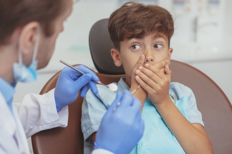 A frightened boy hiding his mouth from a dentist