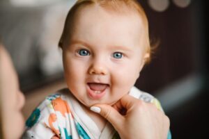 Mother gently pulling baby’s lip to show their first teeth 